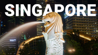 Singapore at night with a lion statue in front of it.