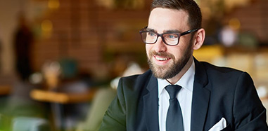 A man wearing glasses and a suit seated at a table while pursuing a Postgraduate Diploma in Entrepreneurship and New Venture Development.